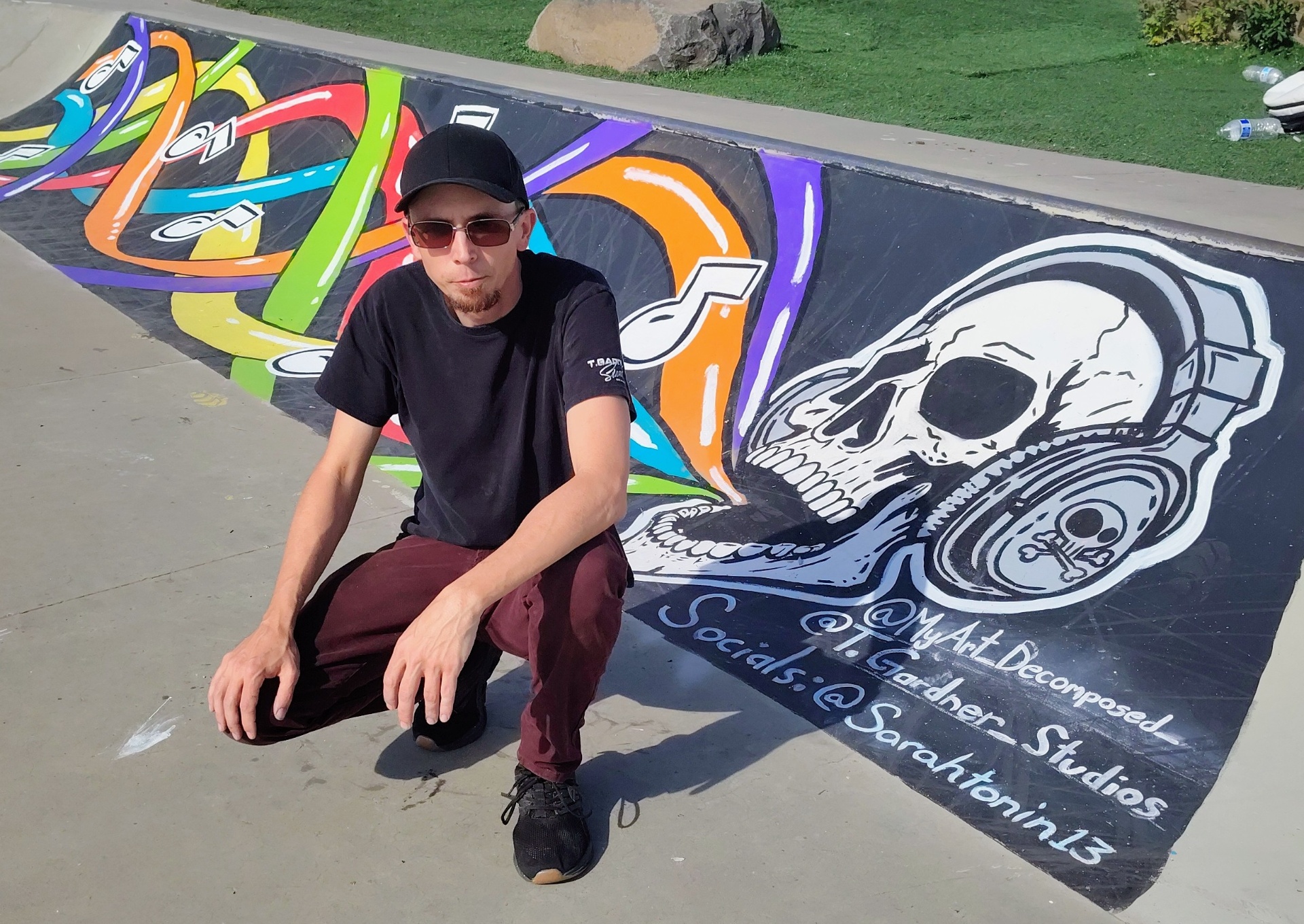 The artist with a finished skatepark mural of a skull in headphones